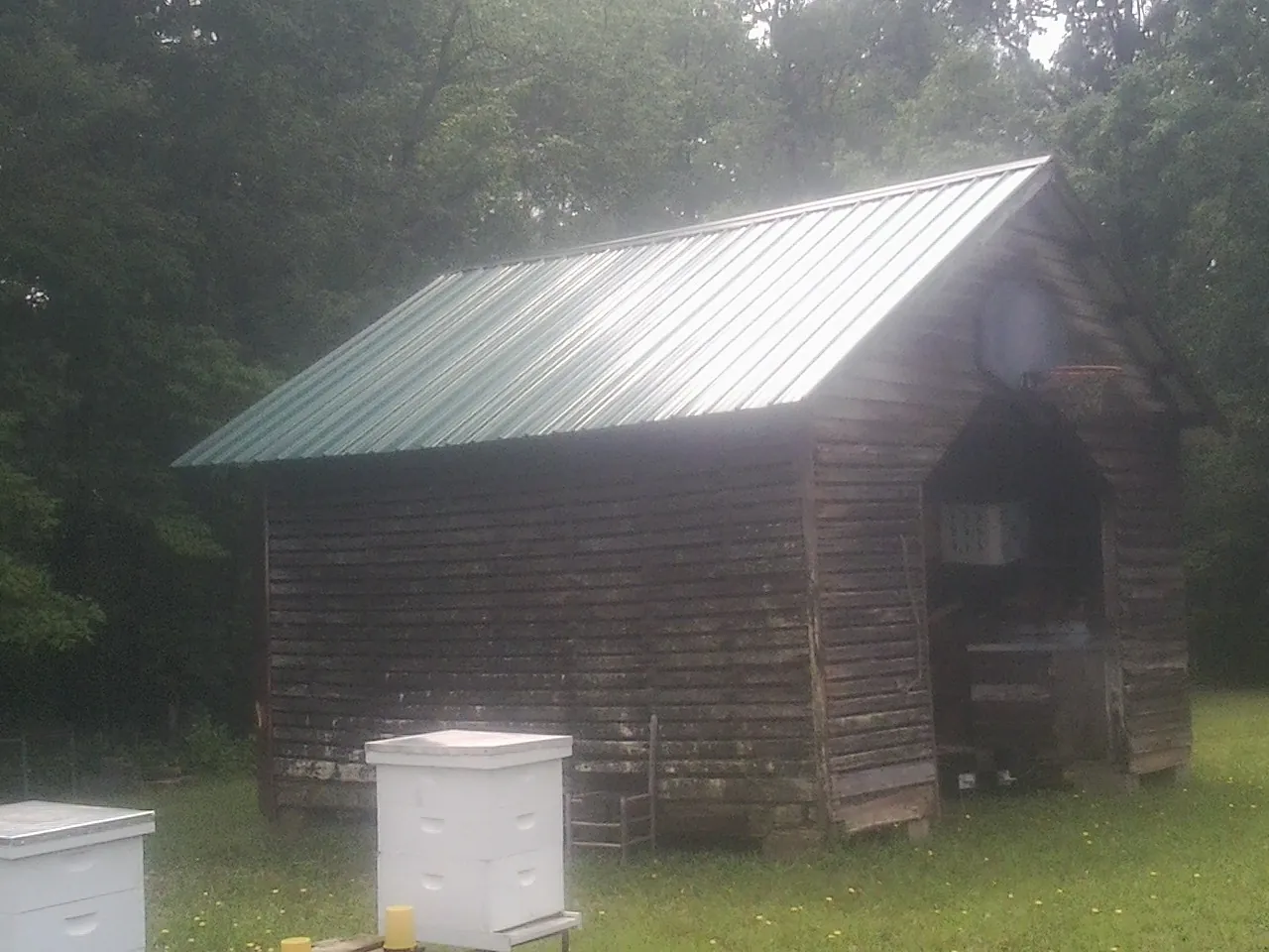 Green metal roof on a weathered barn beside stacked beehives in New Lisbon
